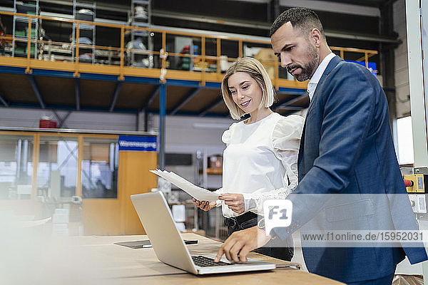 Businessman and young woman with papers and laptop in a factory