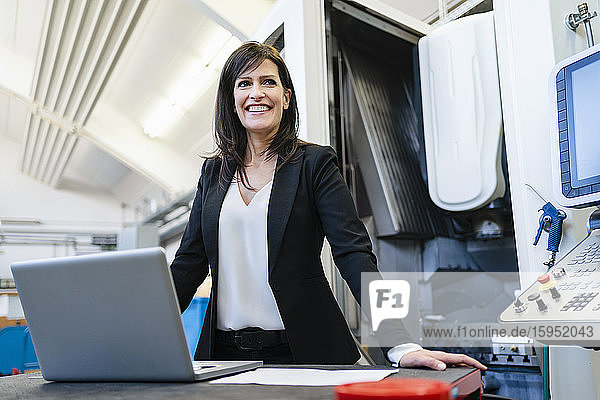 Porträt einer glücklichen Geschäftsfrau mit Laptop in einer Fabrik