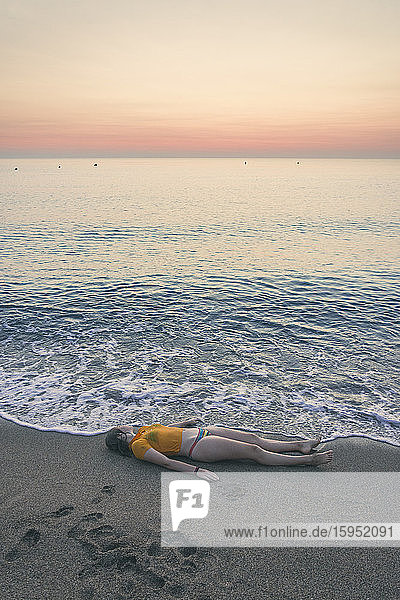 Teenager-Mädchen in voller Länge bei Sonnenaufgang am Strand am Ufer liegend