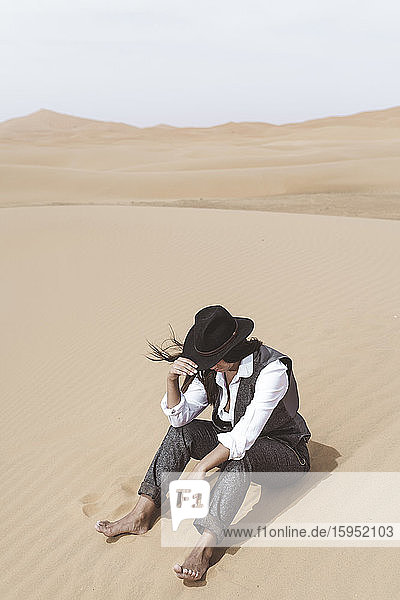 Fashionable young woman sitting barefoot on dune  Merzouga desert  Morocco