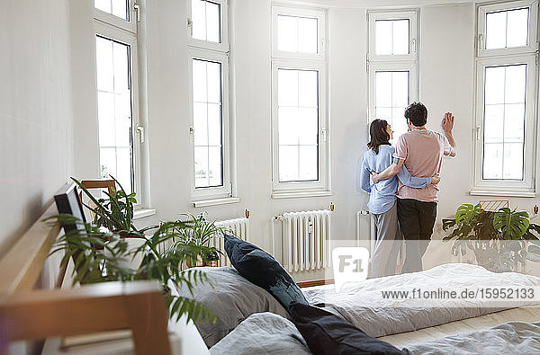 Couple standing at the window at home looking out