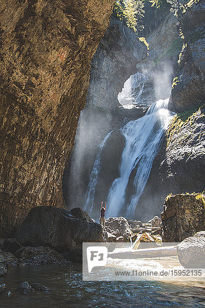 Spanien  Provinz Huesca  Wanderin steht mit erhobenen Armen am Boden eines plätschernden Wasserfalls