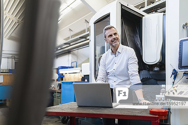 Lächelnder Geschäftsmann mit Laptop in einer Fabrik
