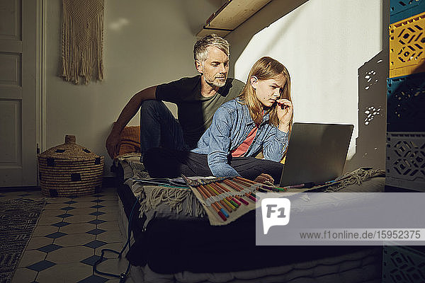Father helping daughter doing homework and using laptop