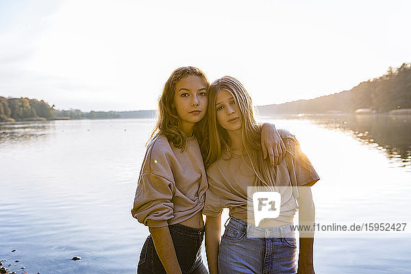 Porträt von Freunden  die bei Sonnenuntergang mit dem Arm um den See herum gegen den See stehen