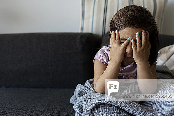 Portrait of girl sitting on couch with obscured face at home