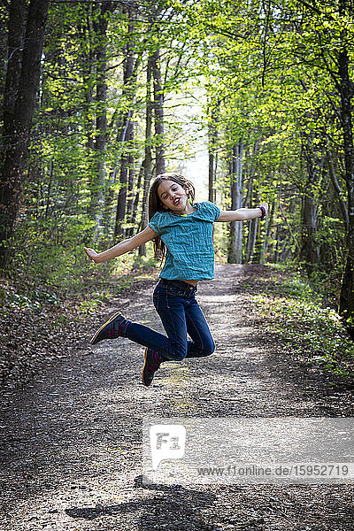 Porträt eines Mädchens  das auf einem Waldweg in die Luft springt