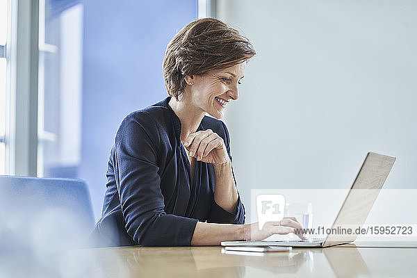 Smiling businesswoman using laptop at desk in office