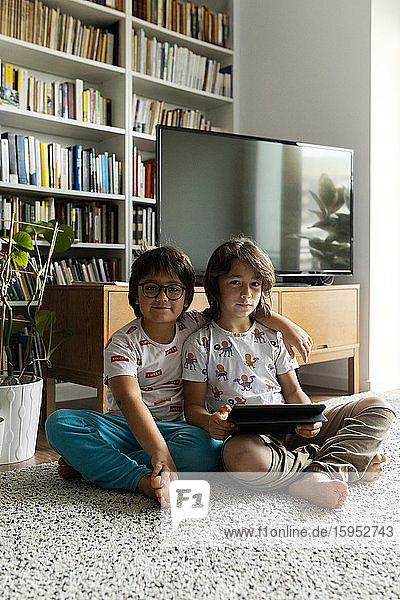 Portrait of two brothers with digital tablet sitting on floor in the living room
