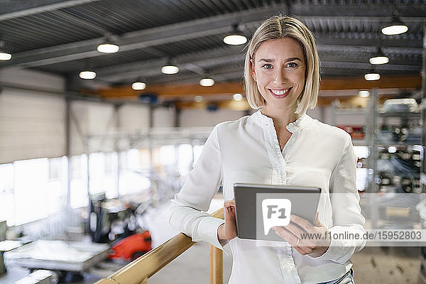 Porträt einer lächelnden jungen Frau mit Tablette in einer Fabrik