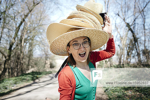 Porträt einer reifen Frau mit einem Stapel Strohhüte auf dem Kopf  die lustige Gesichter zieht