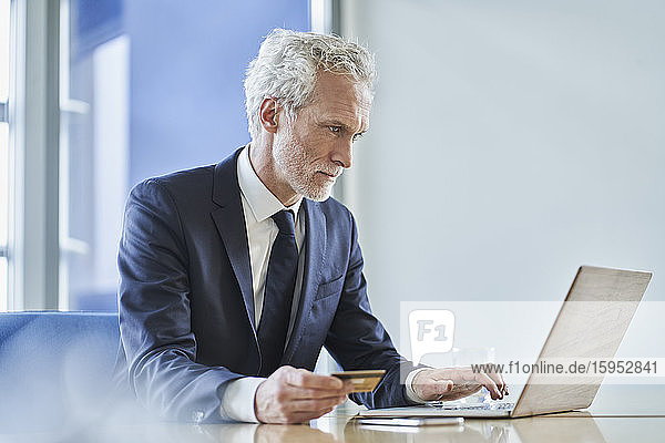 Businessman holding credit card and using laptop at desk in office