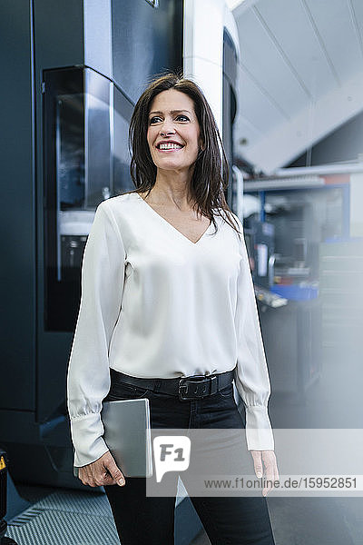 Lächelnde Geschäftsfrau mit Tablette in der Hand in einer Fabrik