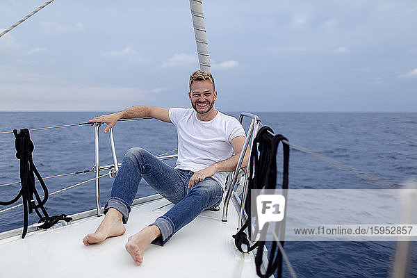 Lächelnder Mann sitzt während der Segelfahrt auf dem Bootsdeck