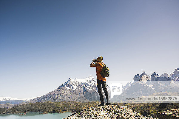 Hiker in mountainscape looking through binoculars at Lago Pehoe in Torres del Paine National Park  Patagonia  Chile