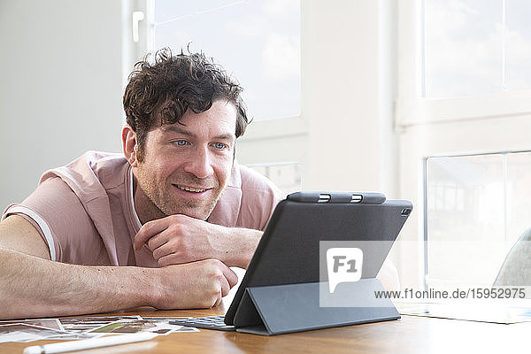 Porträt eines lächelnden Mannes mit Tablette auf dem Tisch zu Hause