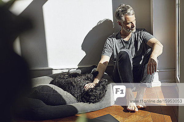 Erwachsener Mann sitzt zu Hause mit Hund auf dem Boden