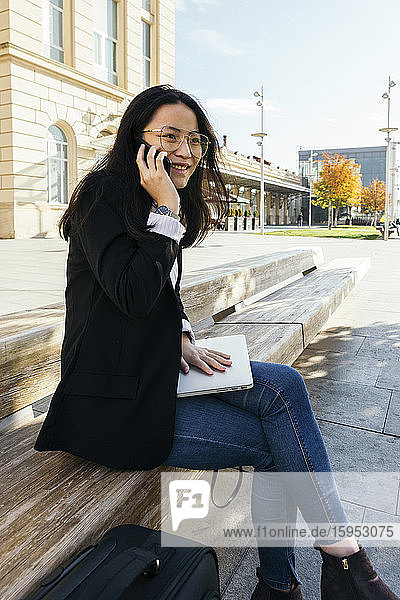Portrait of smiling businesswoman on the phone sitting on bench outdoors