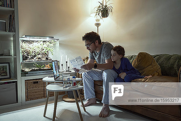 Krankes Mädchen sitzt neben dem Vater mit einem Rezept  während es zu Hause mit dem Arzt über Videoanruf diskutiert