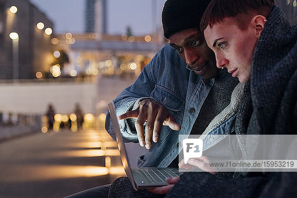 Happy young couple using laptop in the city at dusk