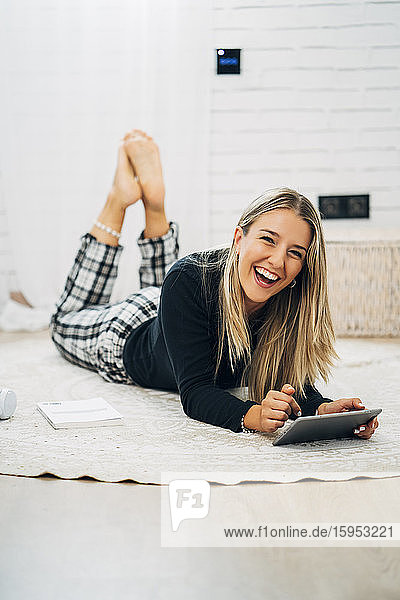 Porträt einer lachenden Frau  die mit einem Mini-Tablett auf dem Boden liegt