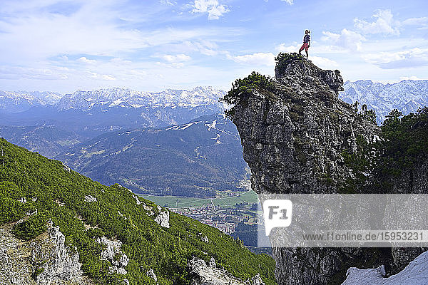 Weibliche Wanderin steht auf felsiger Bergspitze und schaut Landschaft gegen den Himmel