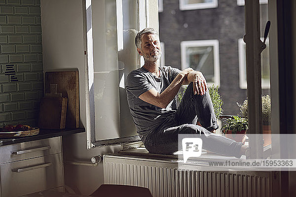 Smiling mature man sitting at the window at home
