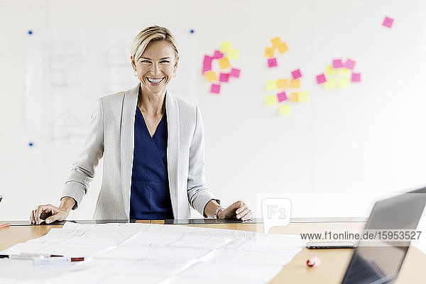 Portrait of happy blond businesswoman in conference room with adhesive notes at whiteboard