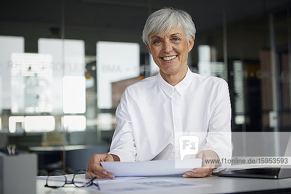 Porträt einer zufriedenen leitenden Geschäftsfrau am Schreibtisch in ihrem Büro