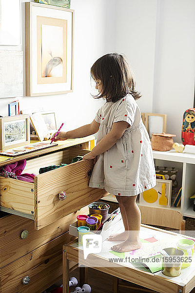 Mädchen zeichnet in voller Länge am Schrank  während sie im Haus auf dem Tisch steht