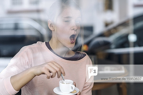 Porträt einer jungen Frau  die hinter einer Fensterscheibe in einem Cafe eine Grimasse zieht