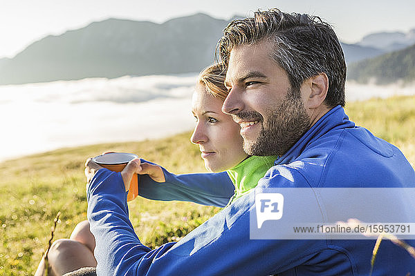 Couple sitting on a meadow in the mountains at dawn  Achenkirch  Austria