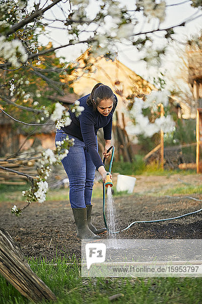 Frau in voller Länge bewässert mit Gartenschlauch