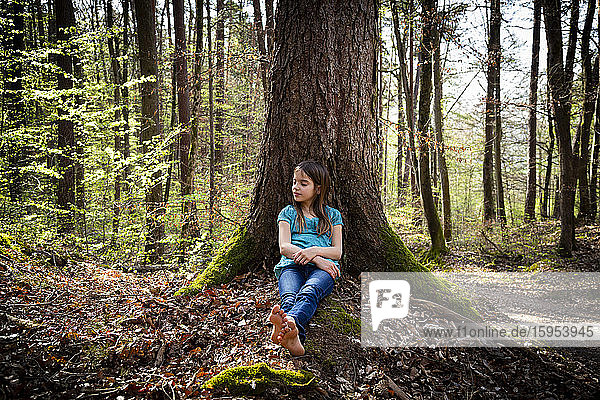 Mädchen mit geschlossenen Augen an Baumstamm gelehnt im Wald