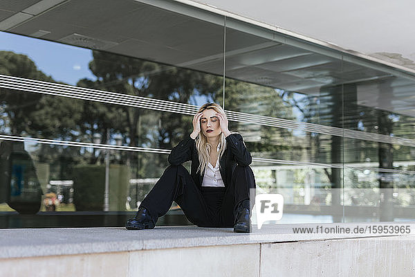 Porträt einer jungen Geschäftsfrau mit gefärbten blonden Haaren vor einem Bürogebäude sitzend