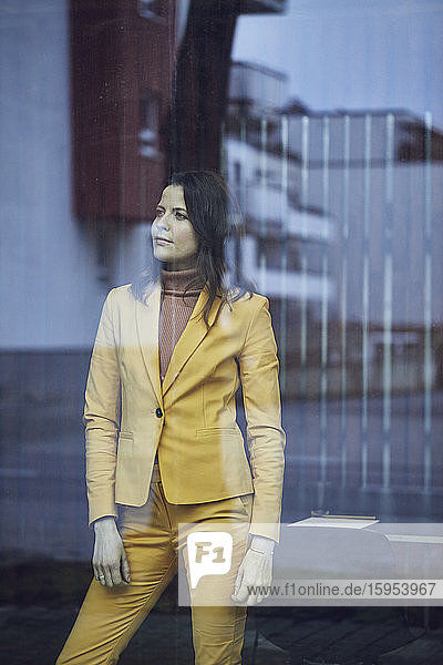 Porträt einer Geschäftsfrau im gelben Anzug hinter einer Fensterscheibe stehend