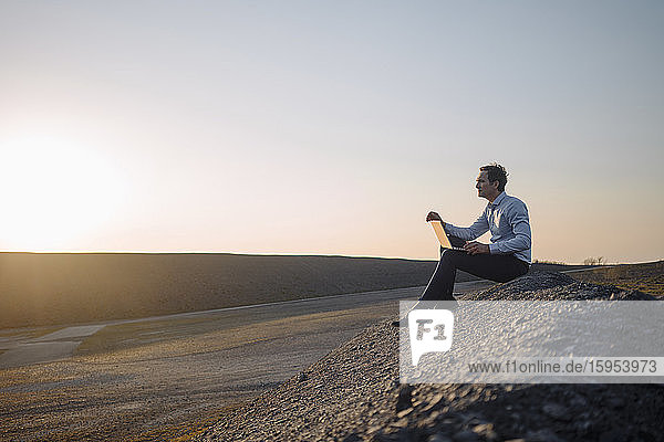 Mature businessman using laptop on a disused mine tip at sunset