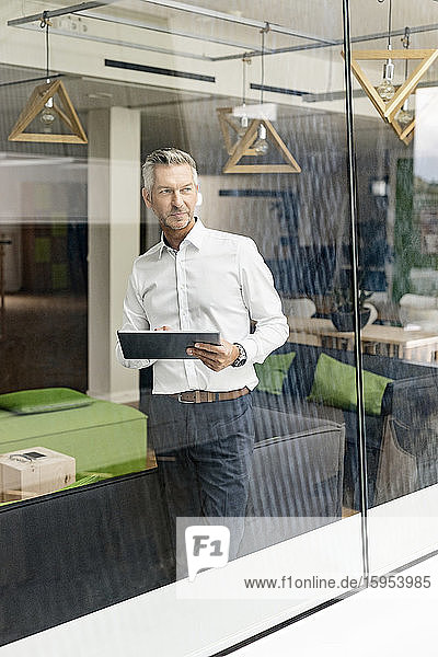Mature businessman in office lounge looking out of window