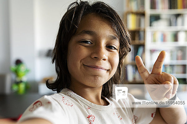 Portrait of smiling boy at home showing victory sign