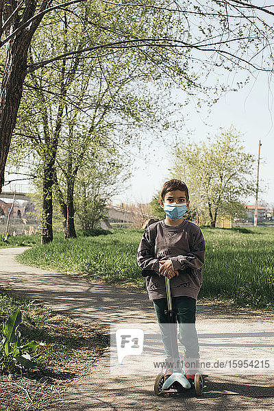 Portrait of boy wearing protective mask with kick scooter in a park