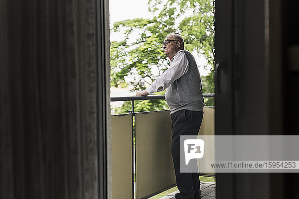Älterer Mann steht auf Balkon und schaut in die Ferne
