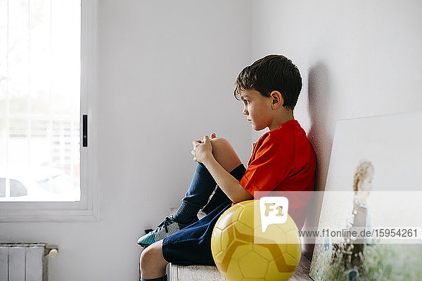 Trauriger Junge mit Fussball auf dem Sideboard sitzend