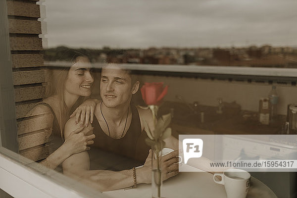 Romantisches junges Paar mit roter Rose hinter Fensterscheibe