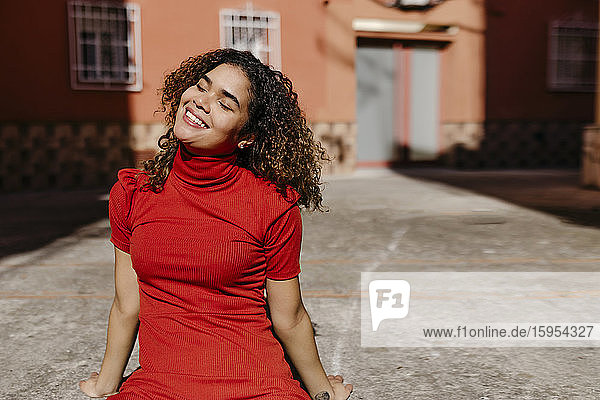 Lächelnde junge Frau in rotem Kleid und auf dem Boden sitzend