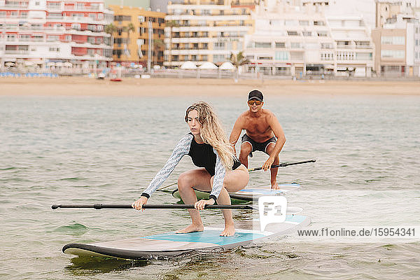 Young woman practicing paddleboarding with instructor on sea