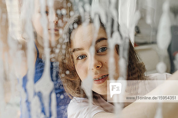 Porträt eines Teenagers,  der durch eine nasse Fensterscheibe schaut