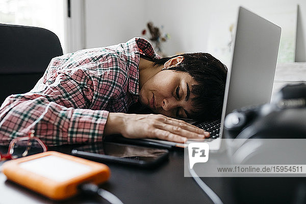 Überarbeitete Frau schläft am Laptop im Heimbüro