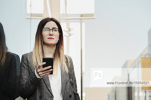 Porträt einer jungen Geschäftsfrau mit Smartphone beim Blick aus der Ferne