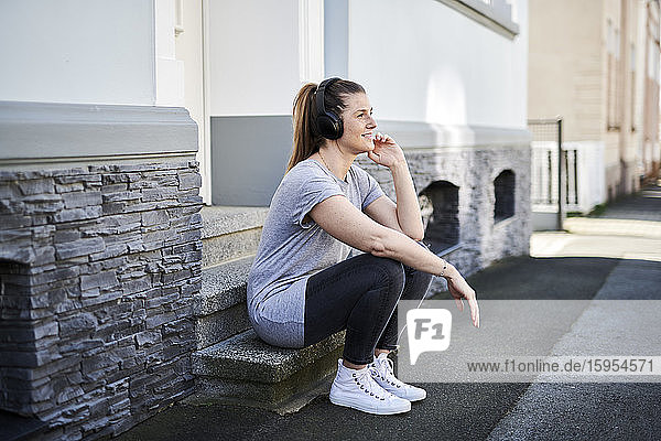 Frau hört Musik über drahtlose Kopfhörer  während sie auf einer Treppe sitzt