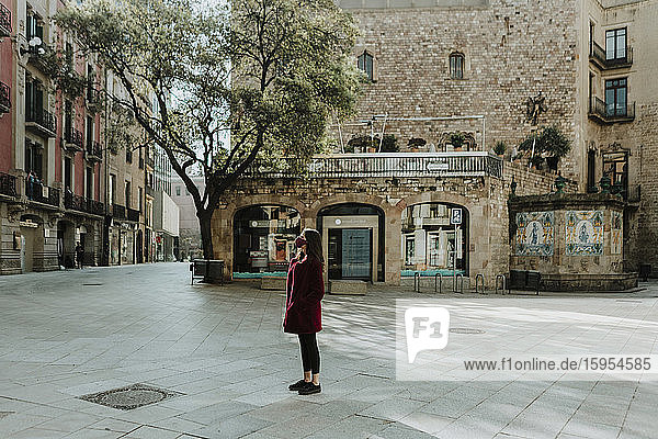 Frau in voller Länge auf einem Fußweg stehend  während sie während der Isolation gegen ein Gebäude im Gotischen Viertel blickte  Barcelona  Spanien